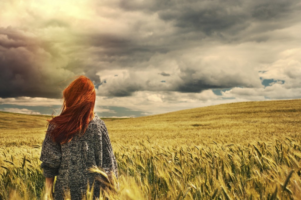 fashion young red hair woman standing back outdoor on breathtaking view of dramatic storm sky in the field