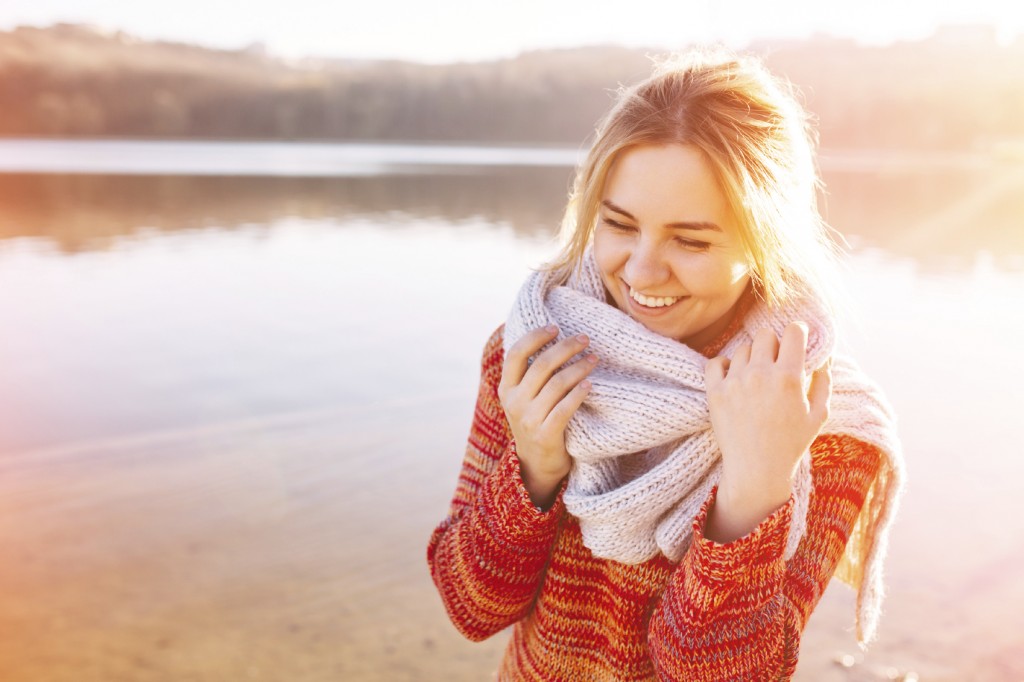 Happy young girl wearing warm clothes standing and smiling by a
