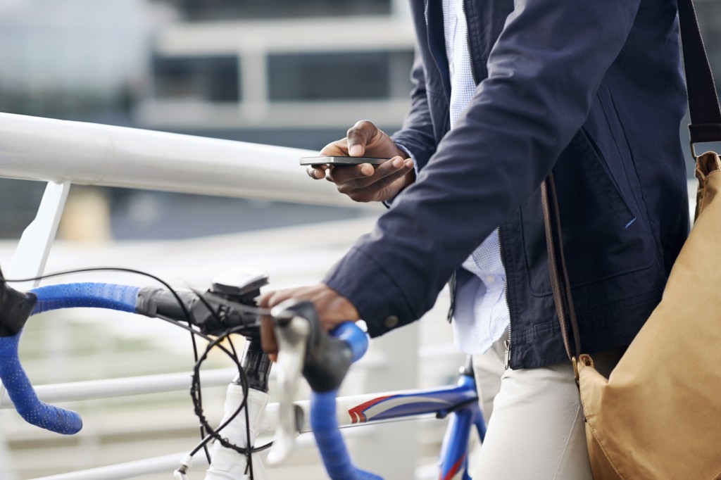 Hipster man with bicycle sending message on mobile cell phone in urban city