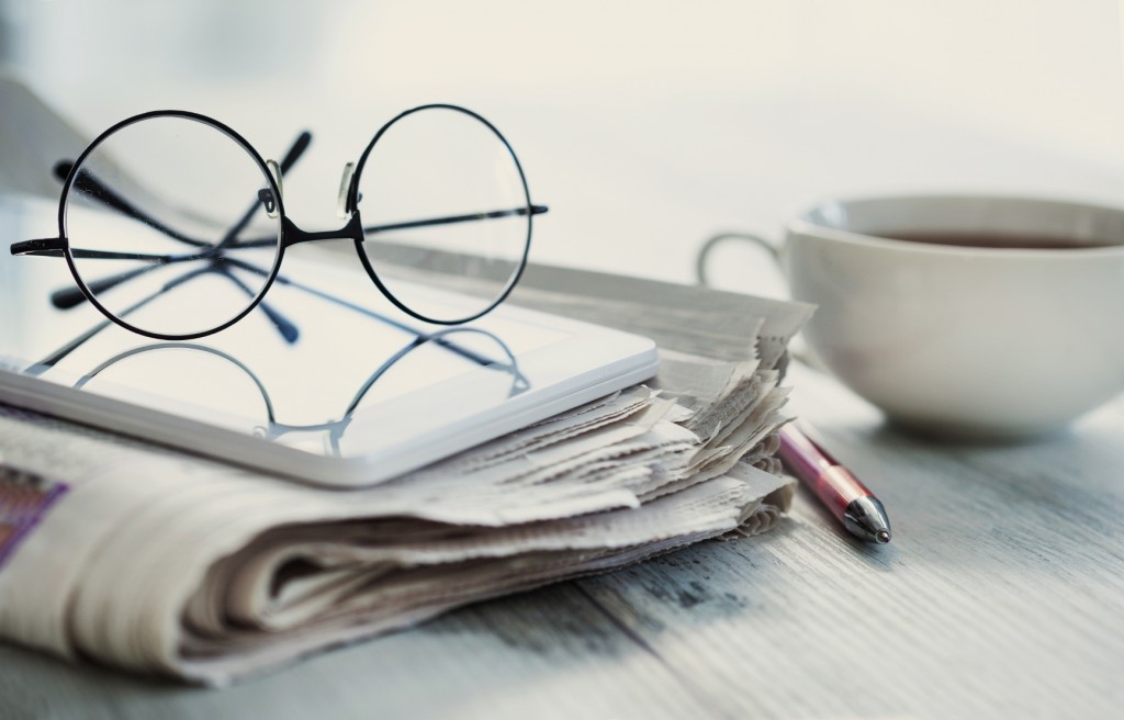 Stack of newspapers, eyeglasses on table -