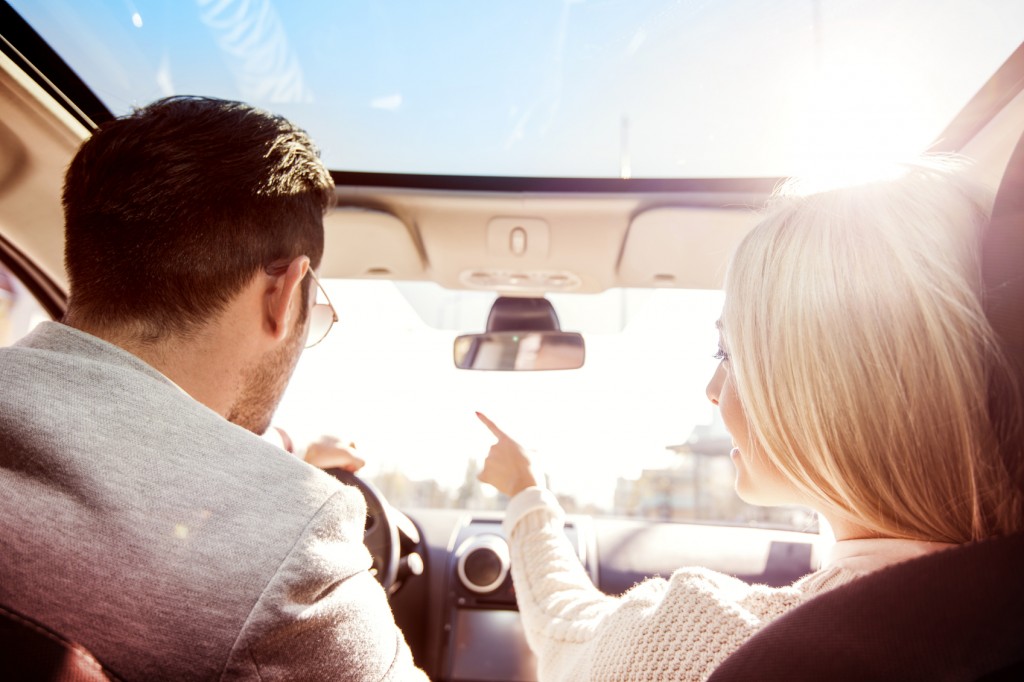 A young woman and a young man are laughing in the car, enjoying in the road trip. The man is driving.