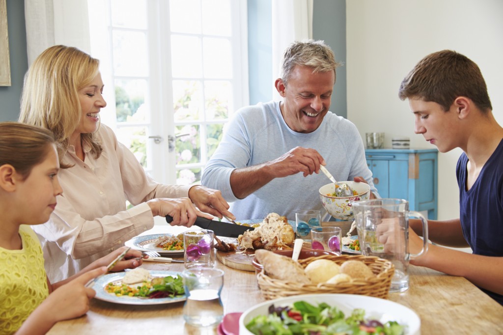 Family Sitting At Table Enjoying Meal At Home Together
