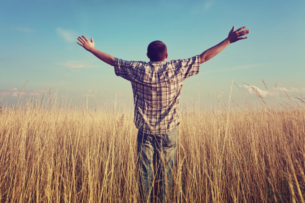 Man with arms raised in field praying