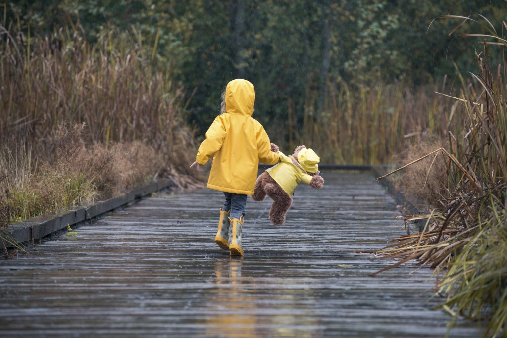 Girl with teddy bear wearing yellow raincoats walking in rain