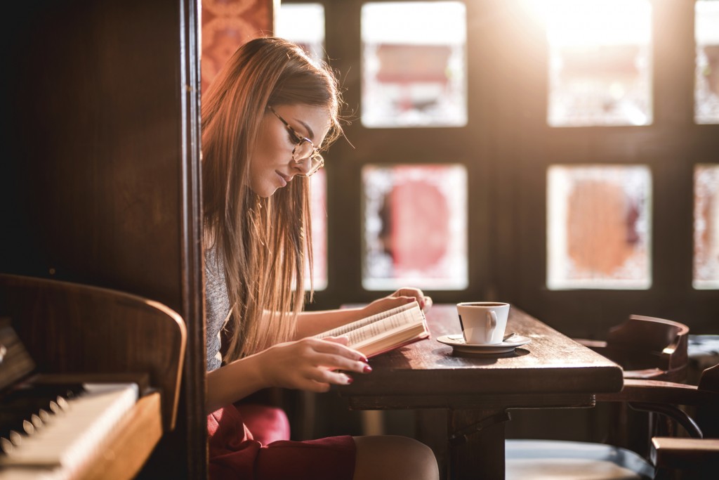 Portrait of young woman having coffee break. She is wearing eyeglasses and studying while sitting alone in coffee shop.