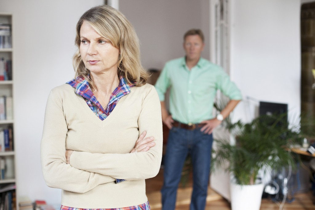 Upset woman standing with man in background at home. Mature couple having relationship difficulties.