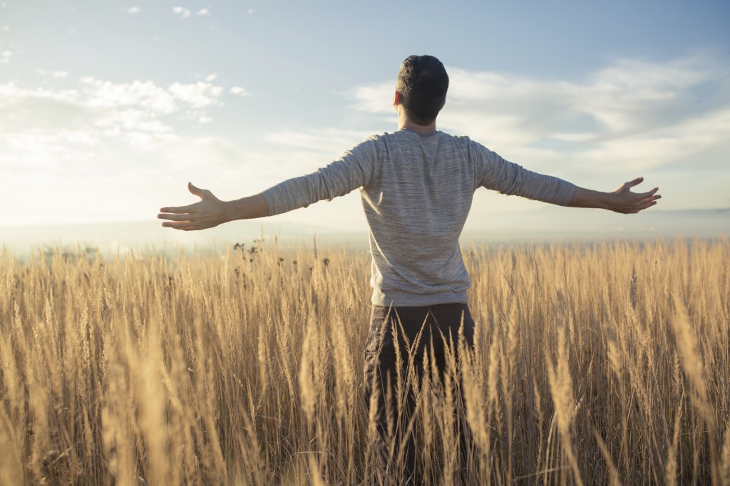 Young caucasian man standing in the middle of a prairie with his arms outstretched, enjoying a beautiful sunny day in the nature.