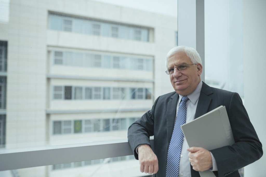 Smiling confident businessman standing at the office window and looking at the camera
