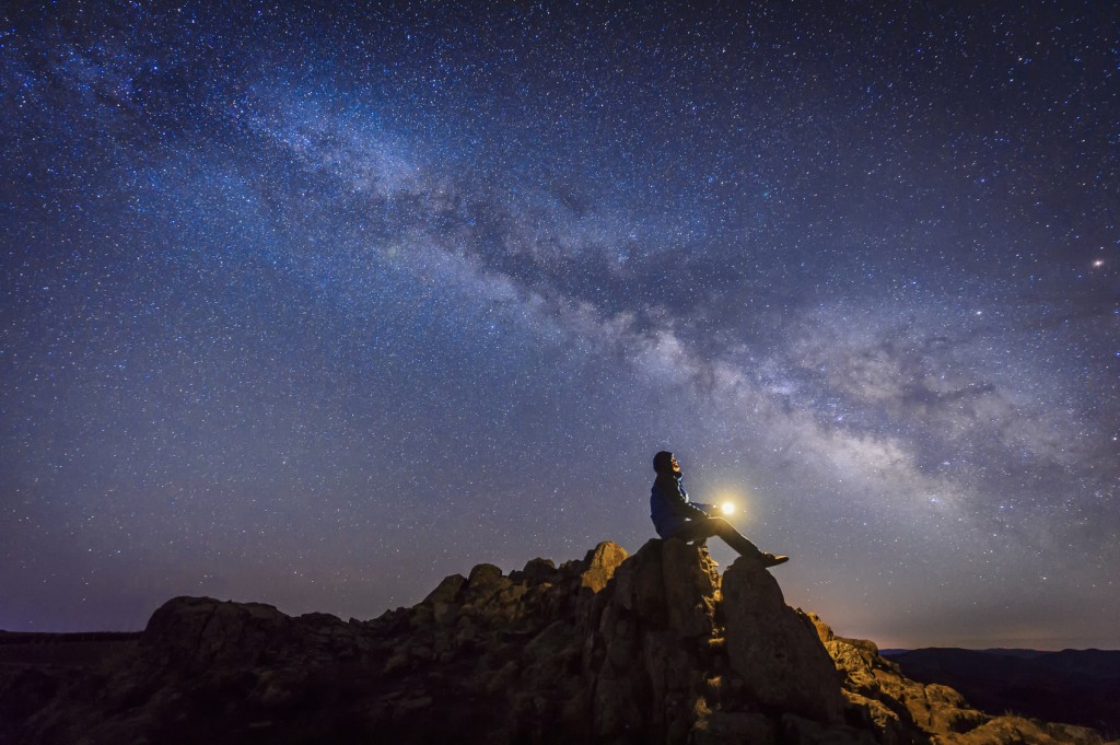 Man sitting under The Milky Way Galaxy with light on his hands.