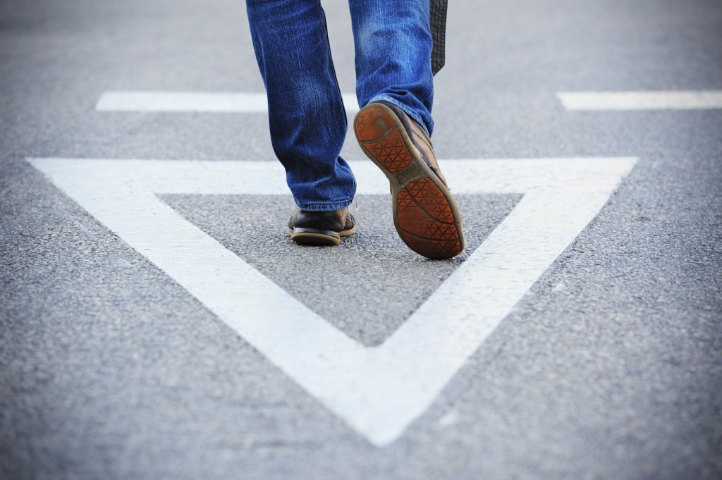 Close up of Man walking in the middle of the road. Alone. Painted triangle. Close up on feet / shoes.