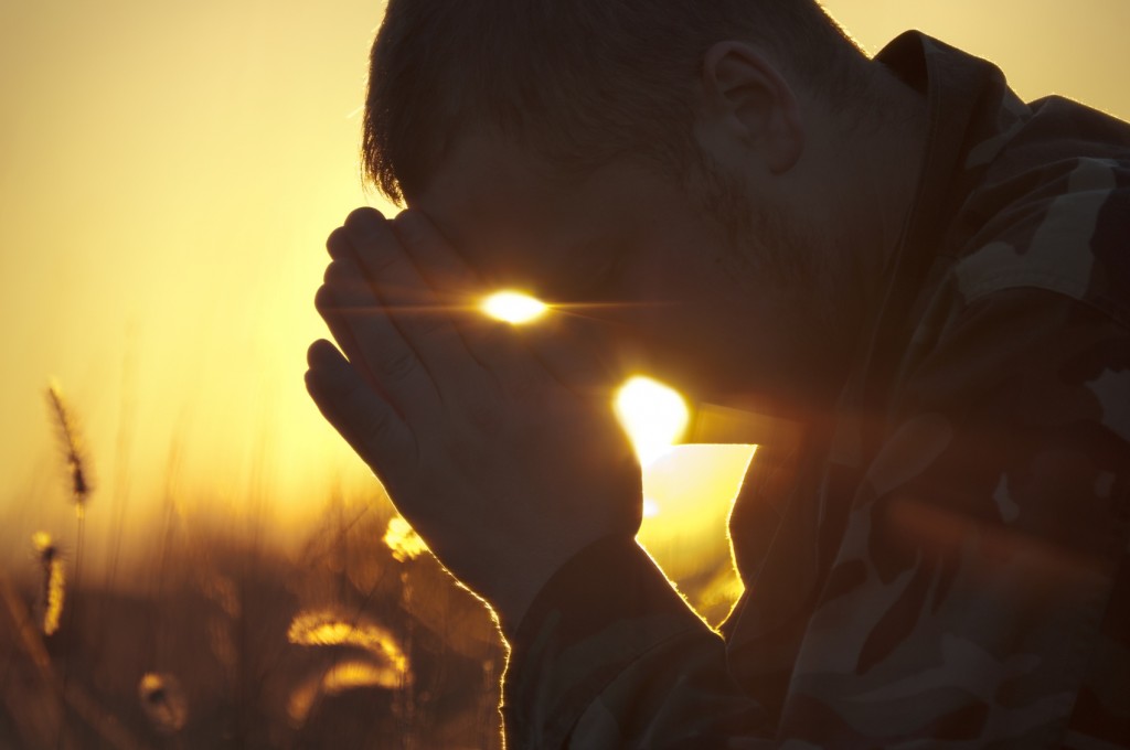 Man Praying Outside in Field at Sunset