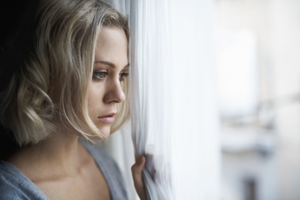 young blonde woman looking out of her window sadly