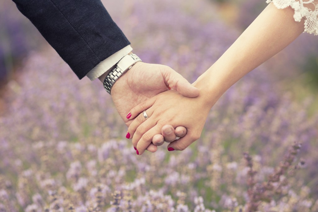 Close up of a male and female hands holding each other. Lavender field in the back.