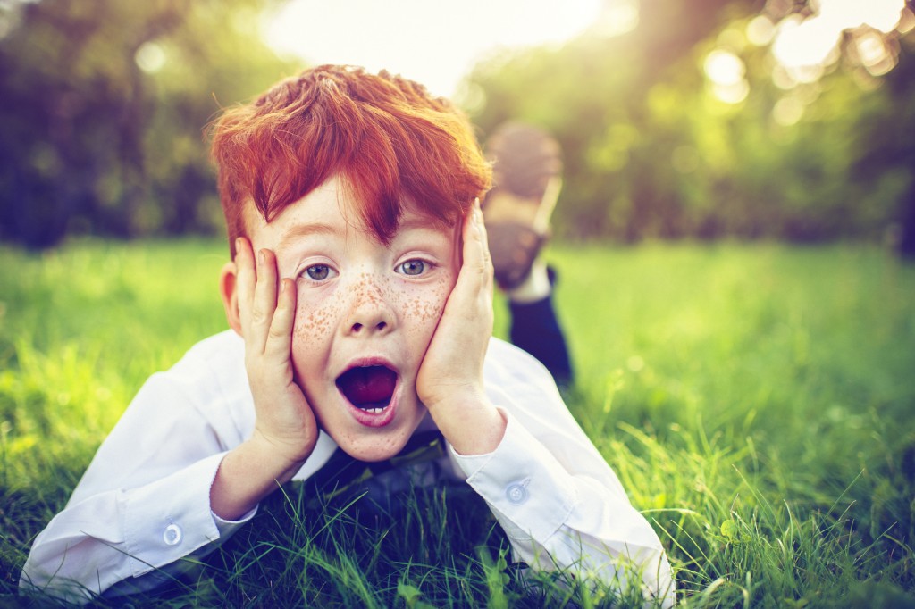 Surprised child with red hair and freckles in park in summer