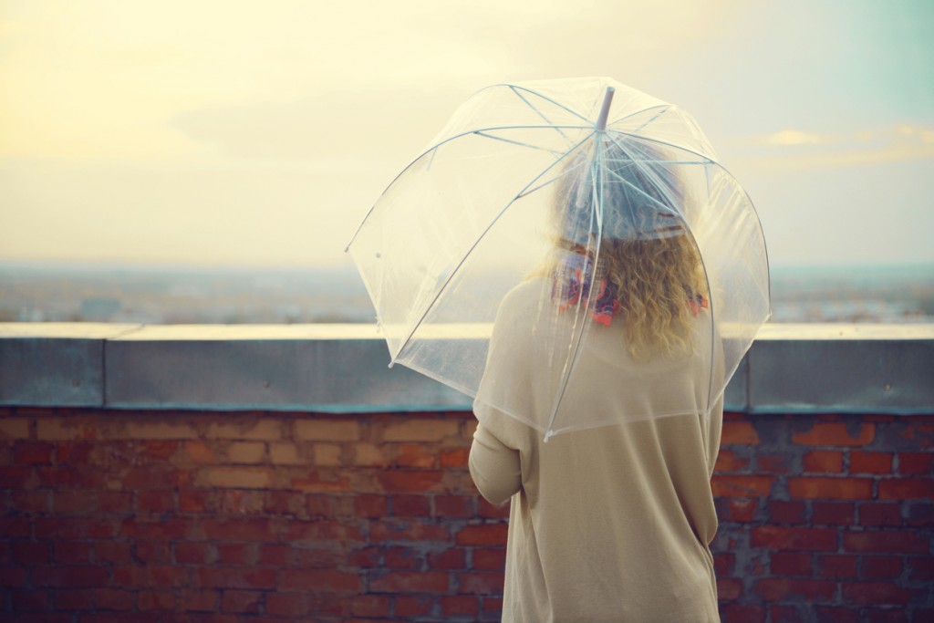 young woman standing on a roof under a transparent umbrella and looking at the horizon