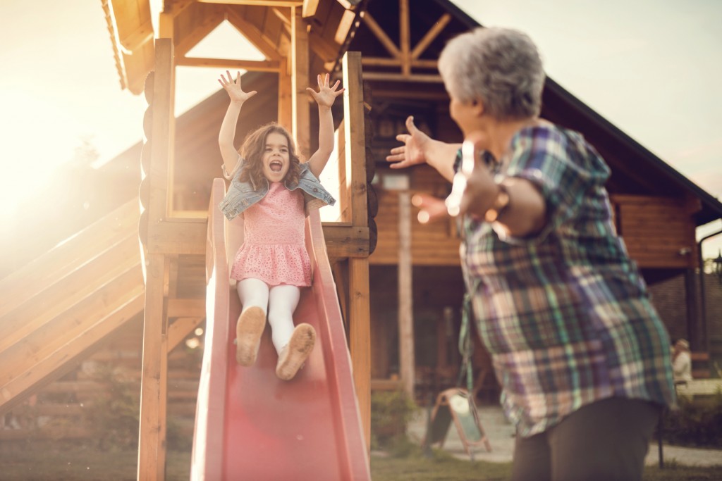 Little girl sliding and having fun outdoors with her grandmother.