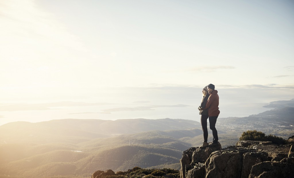 Shot of a young couple looking down at the view from the top of a mountain