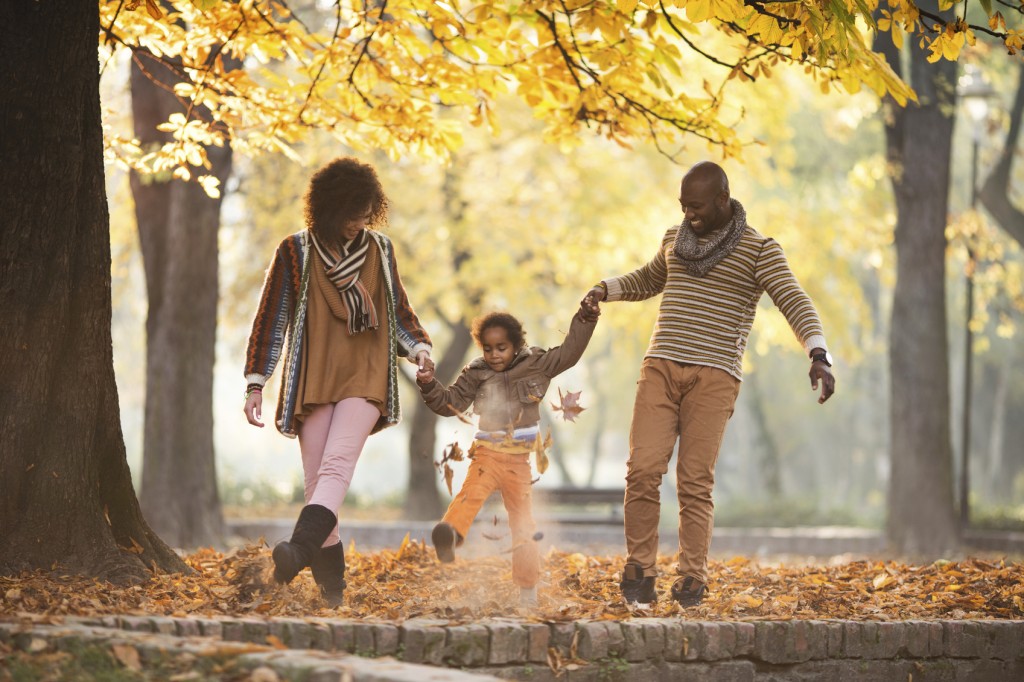 African American family holding hands and having fun while walking in autumn park.