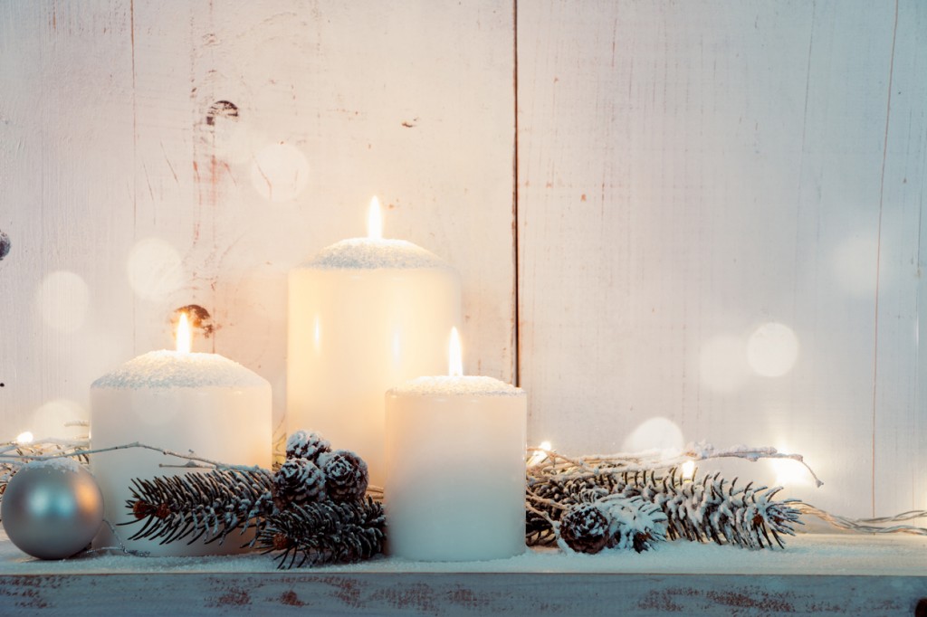 Christmas candles and snowy fir branches over white wooden background with lights