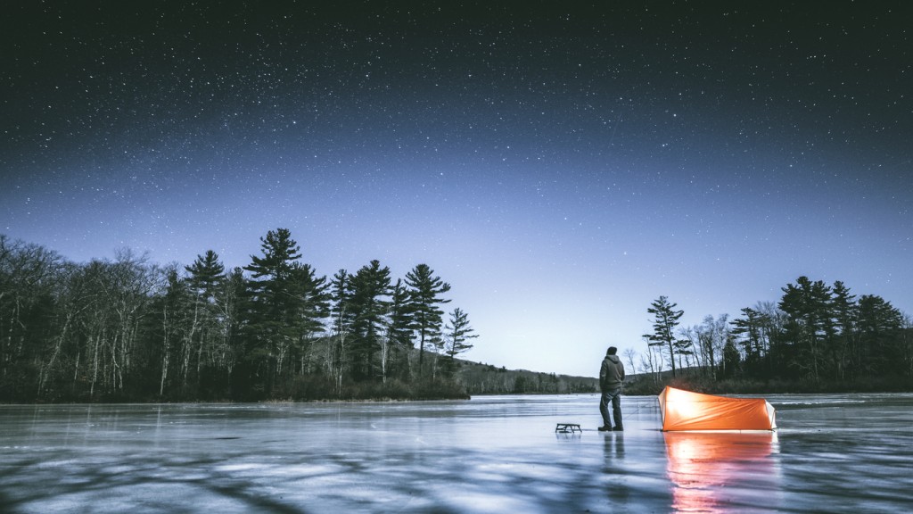 Man standing on the frozen lake in Connecticut's dark and wild north west corner of the state, next to his tent looking up observing stars on cold full moon winter night.