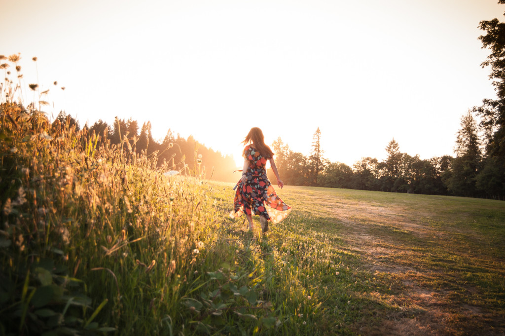 A beautiful woman is walking through a meadow. She's alone in a peaceful natural setting, walking towards the setting sun. The meadow is located in Sandy, Oregon.