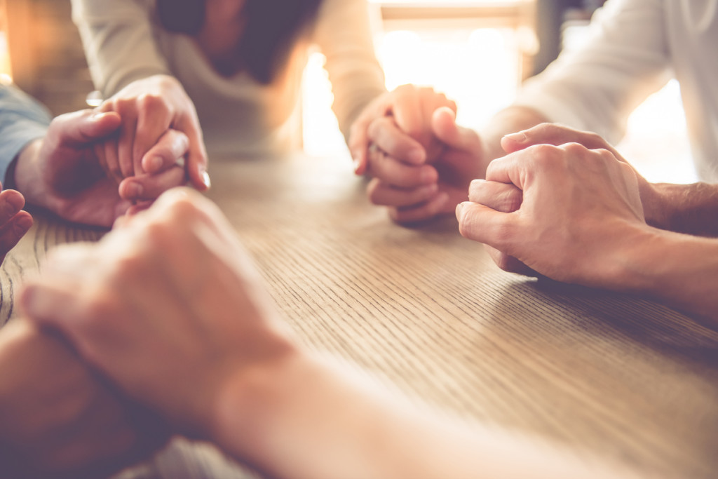 Cropped image of beautiful business team holding hands and praying while sitting in office