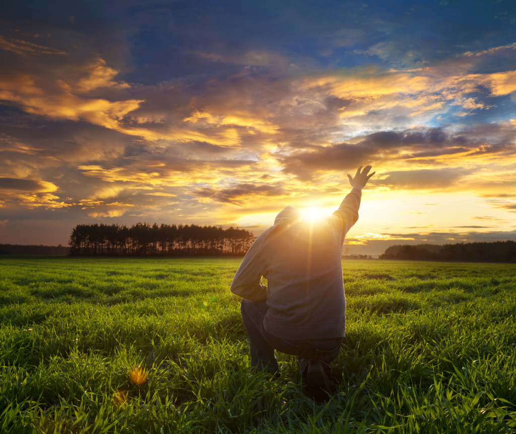 Man on meadow praying to god facing the sun