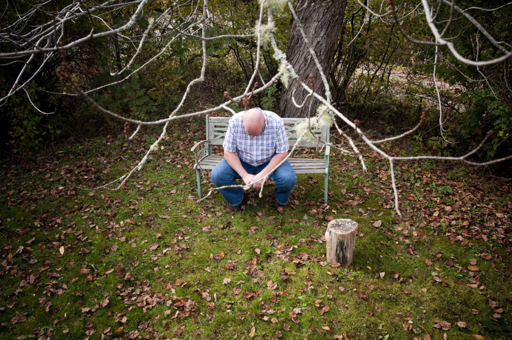 A depressed aging man sitting on a bench in Fall with his head hung low.