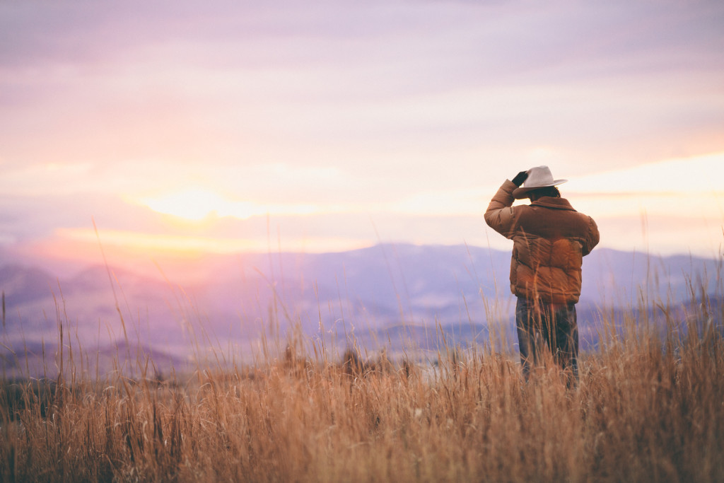 Cowboy talks on phone while watching sunset over mountains