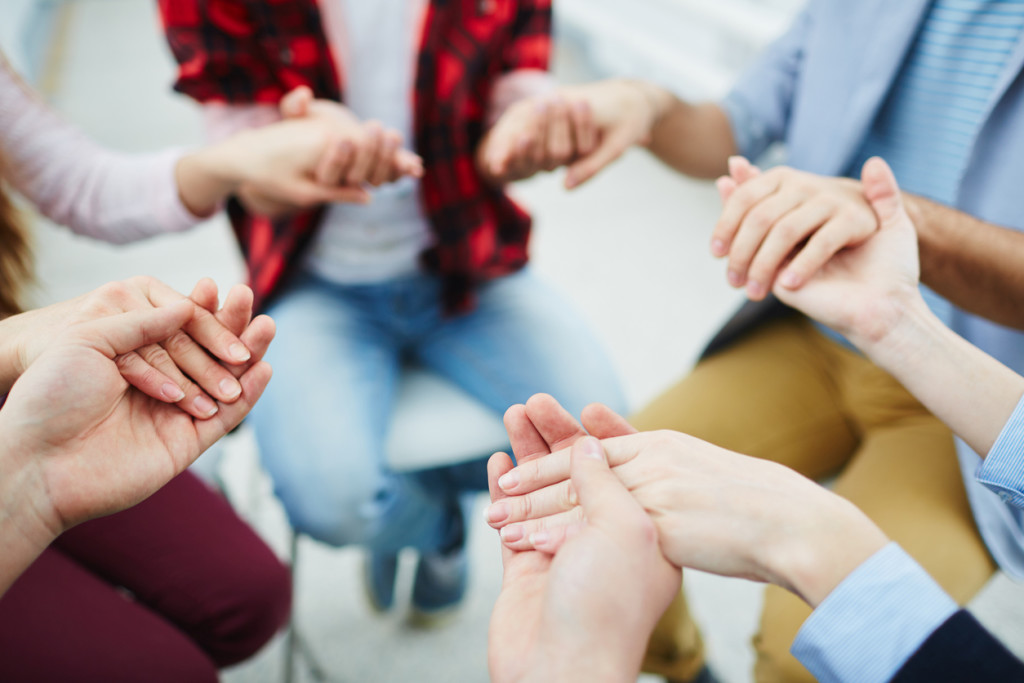 Circle of groupmates holding by hands at psychological session