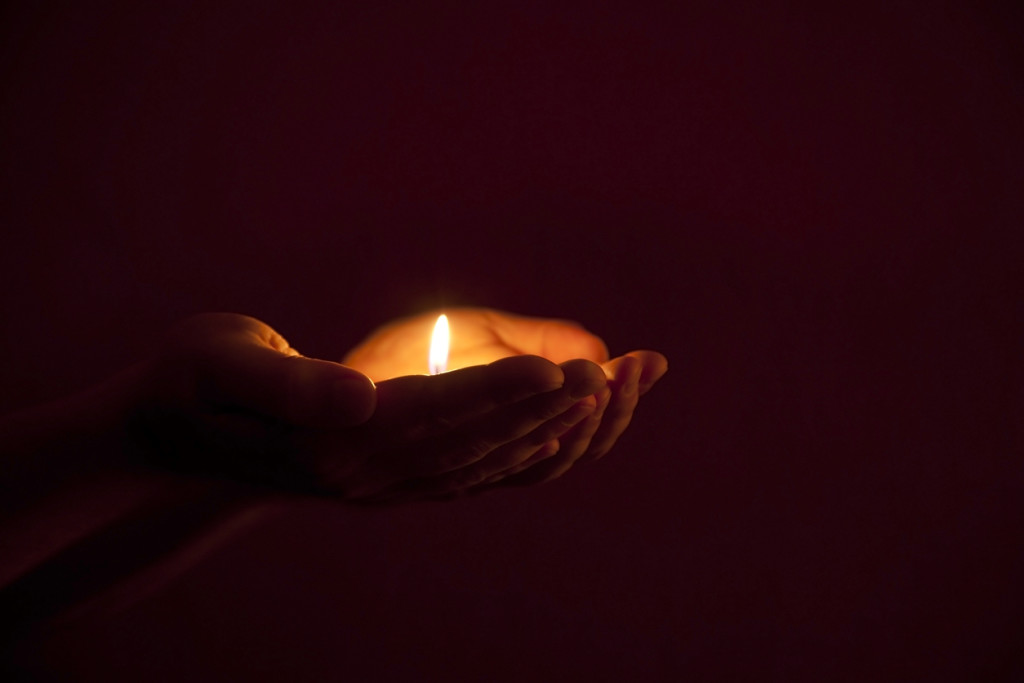 burning candle in human hands in darkness