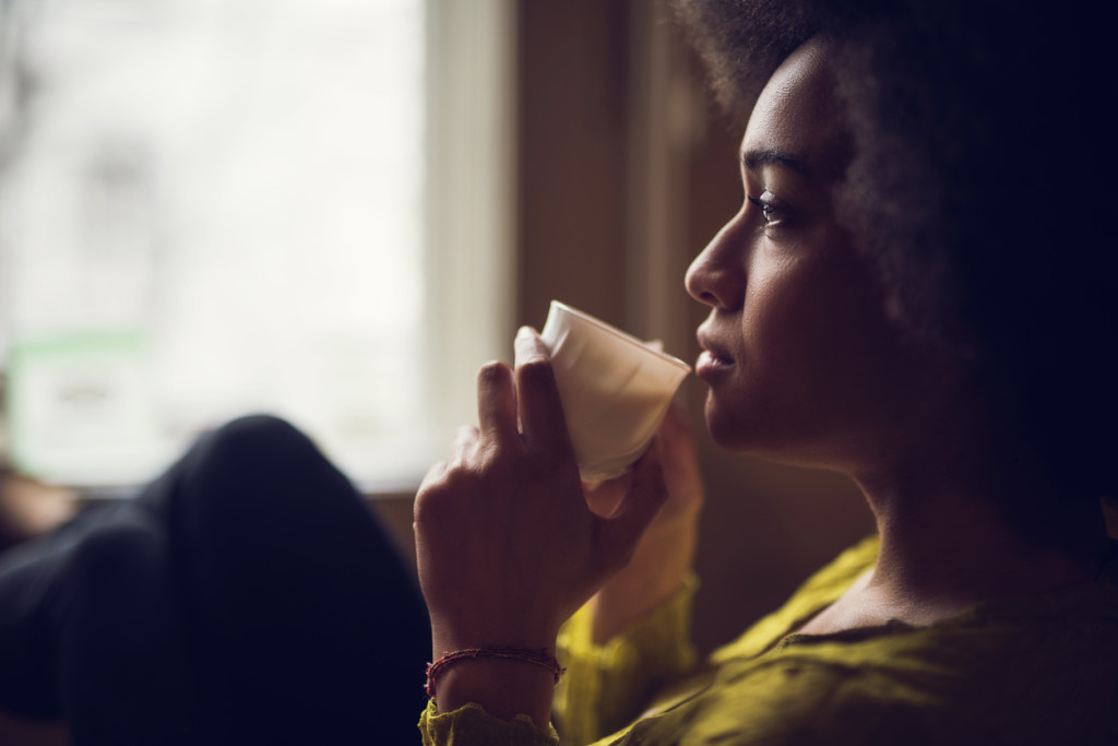 Young pensive African American woman drinking coffee and looking away.