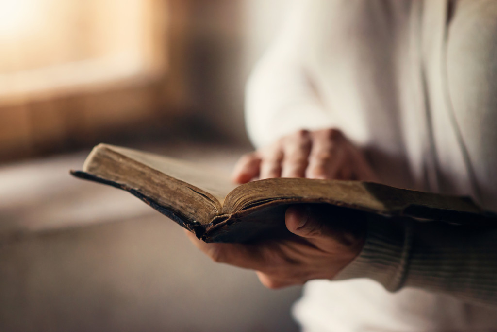 Unrecognizable woman holding an open bible in her hands and praying