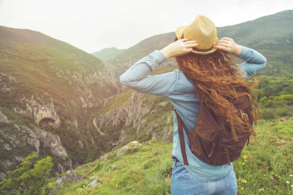 Young beautiful woman with a straw hat and a backpack standing on the top of the gorge and enjoying the view
