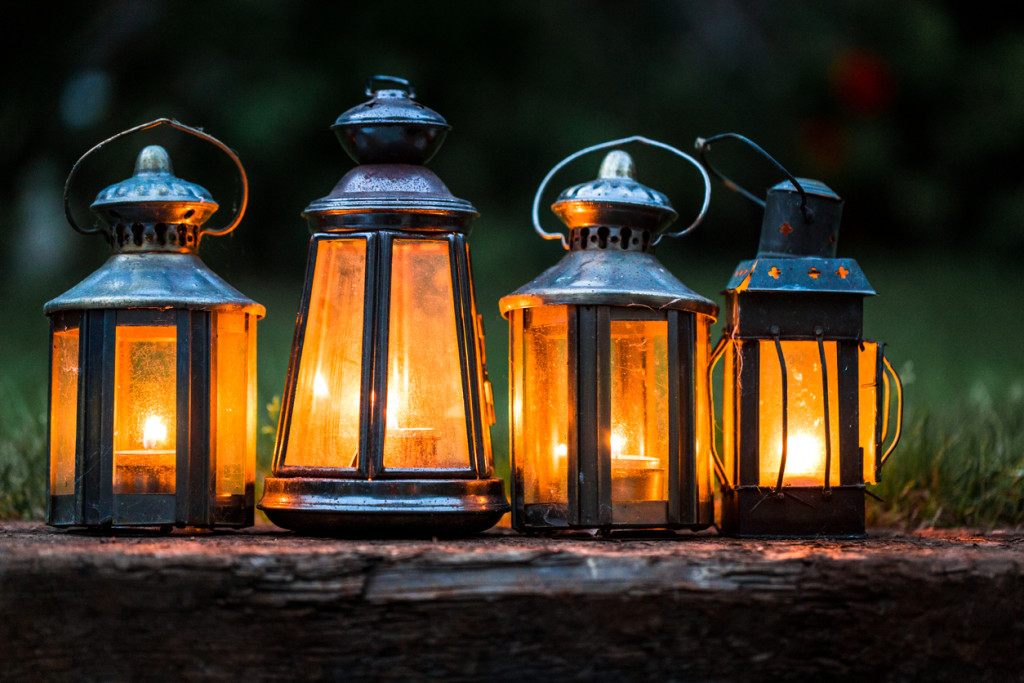 Four illuminated lanterns in a row outdoors in garden