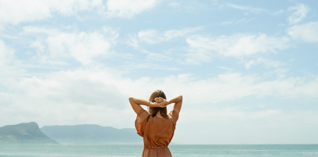 Rearview shot of a woman looking out at the ocean with sky above