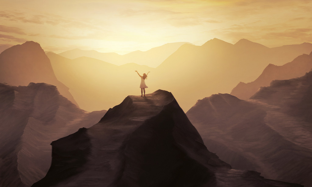 A woman stands alone on a mountain with her hands in praise.