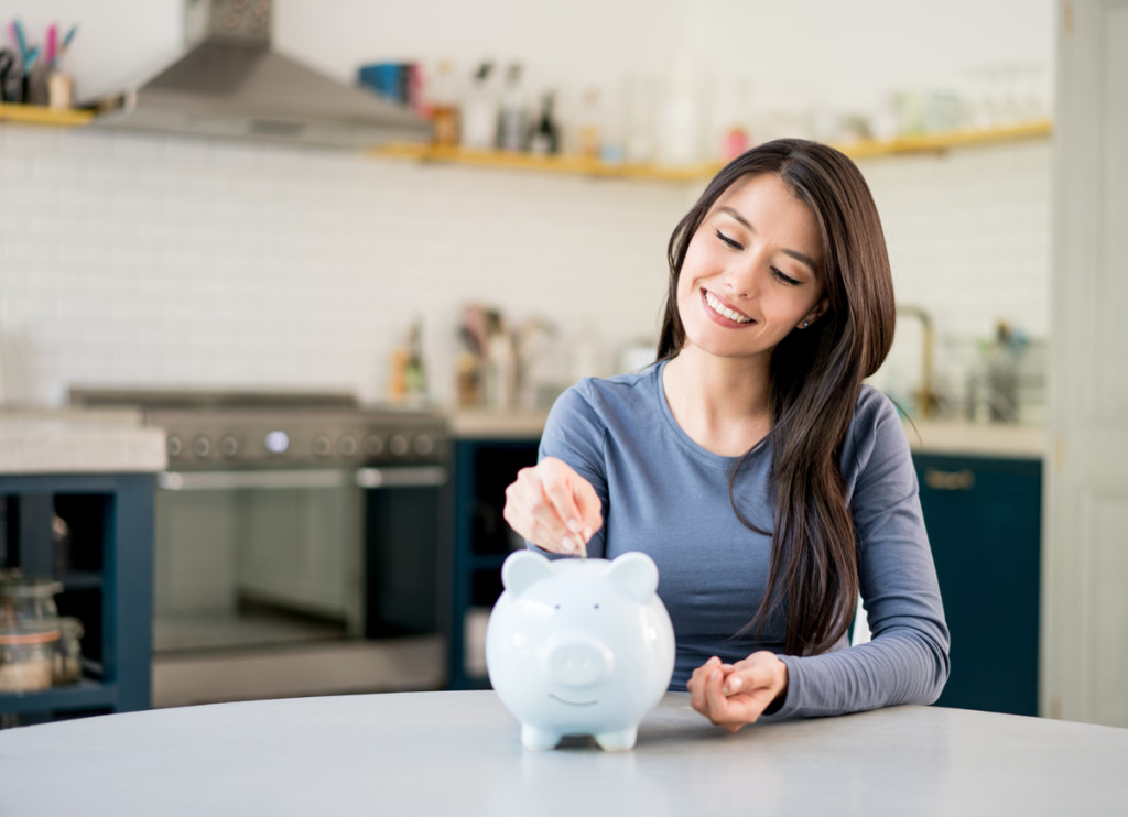 Portrait of a Latin American woman saving money in a piggybank and looking very happy