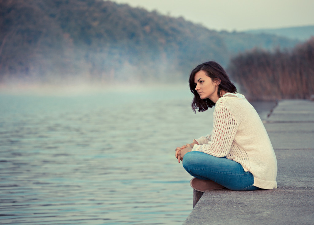 Young woman sitting by lake in the early morning.