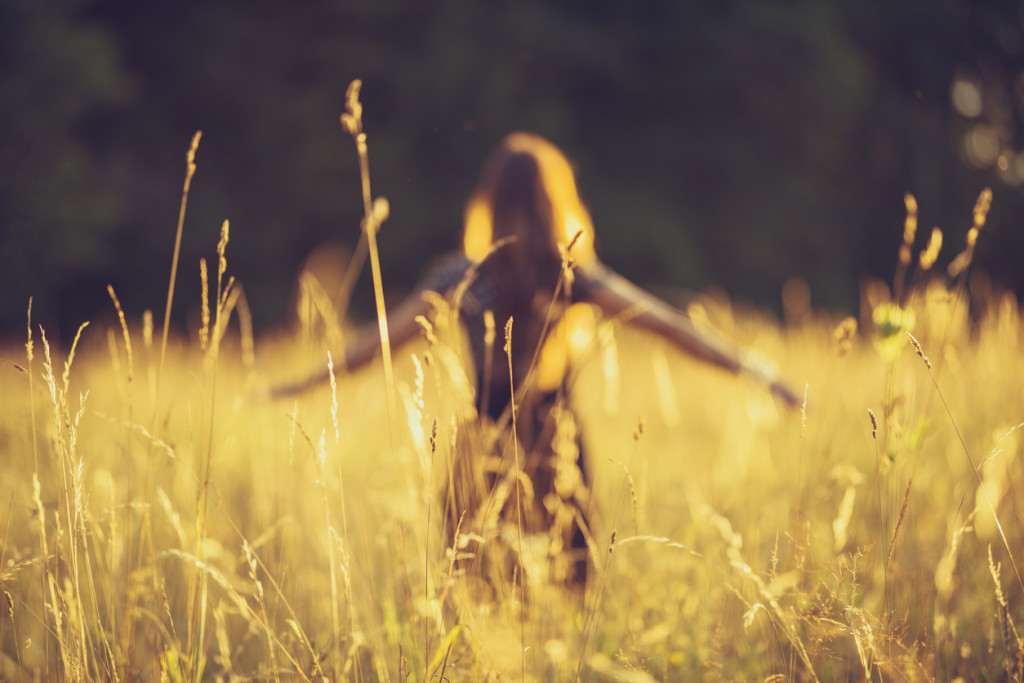 a young women walk through the high grass. the evening sun is shining very bright