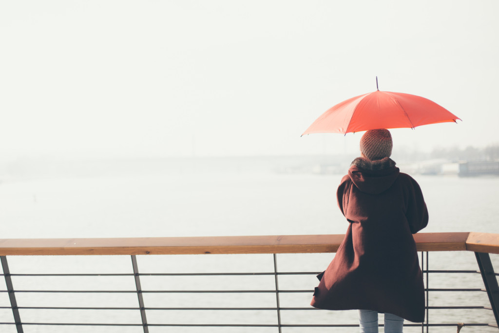 Woman standing at the balcony looking at the river and holding umbrella