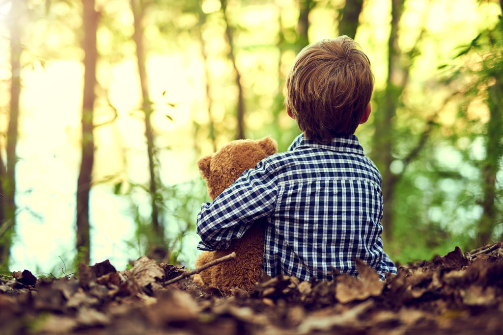 Shot of a little boy sitting in the forest with his teddy bear
