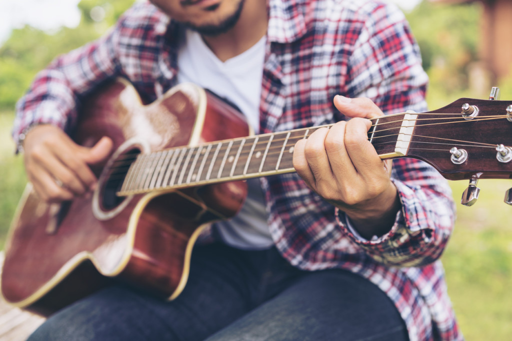 Man 's hand playing guitar, sitting on green grass.