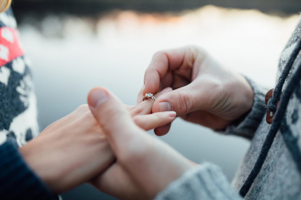 Picture of man putting engagement silver ring on woman hand, outdoor. Seaor river background.