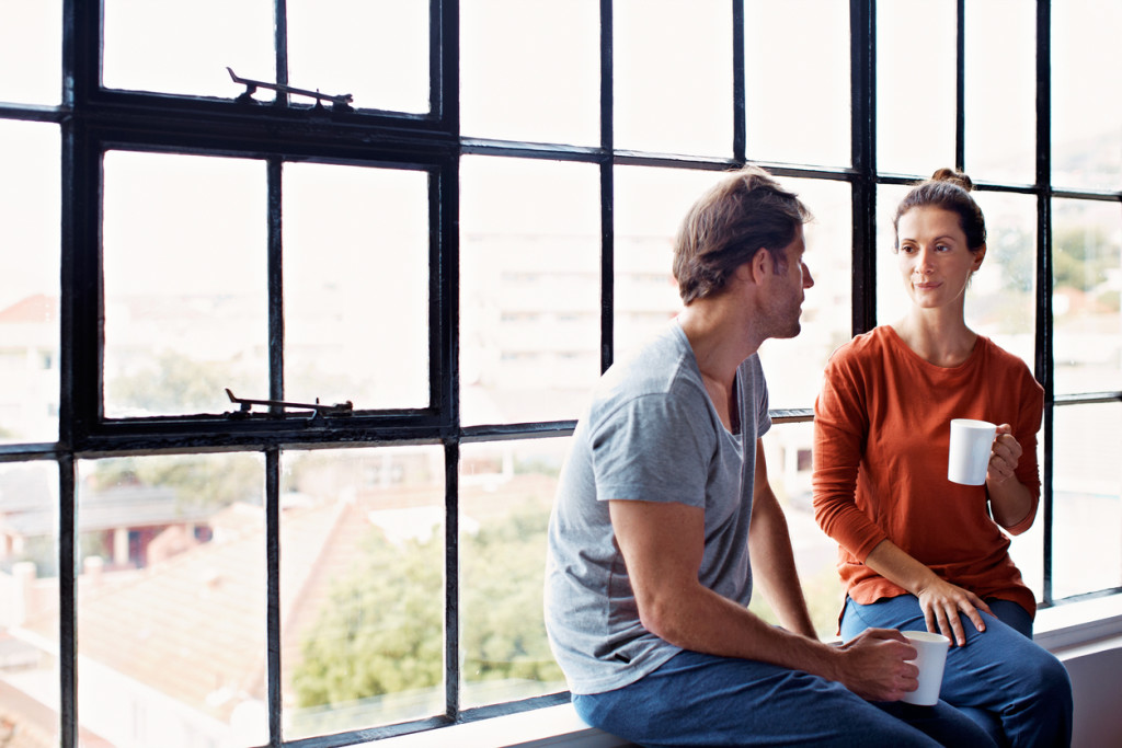 Shot of a happy mature couple sitting on a window sill at home drinking coffee and talking together