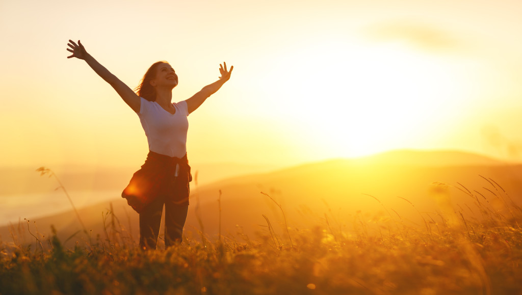 Happy woman on the sunset in nature in summer with open hands