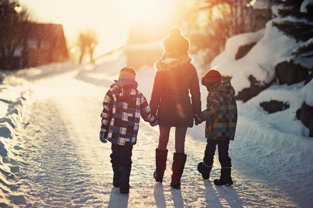 Brothers and sister walking on road on sunny winter evening.