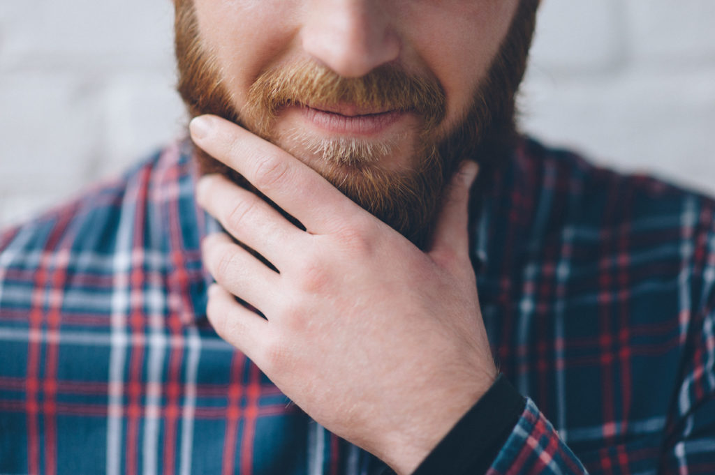 young man in a flannel shirt touches with hand his beard