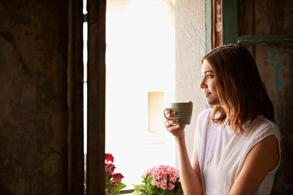 Shot of a young woman drinking a cup of coffee while looking out of a window