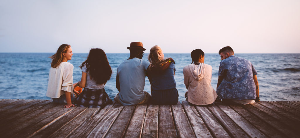 Young multi-ethnic couples and friends sitting on wooden jetty together